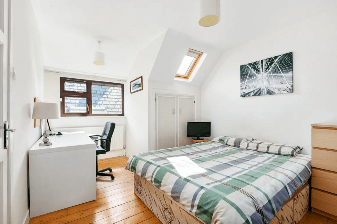 bedroom 3 with white walls, timber flooring, large bed, white study desk, sky light window and small window with view of adjacent property