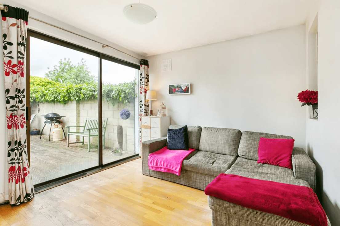 Family Room with white walls and ceiling, timber flooring, large sliding doors to the rear garden and a coffee-coloured sofa.