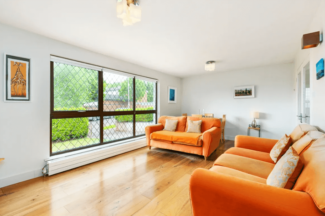 129 Wesbury Stillorgan Dublin Living Room with white walls and ceiling, timber flooring, large lattice-style window to the front garden, and an orange-coloured sofa.