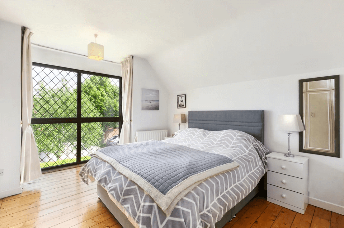 129 Wesbury Stillorgan Dublin Principal bedroom with white ceiling, large bed, timber flooring, large bed and medium-sized window with view of garden