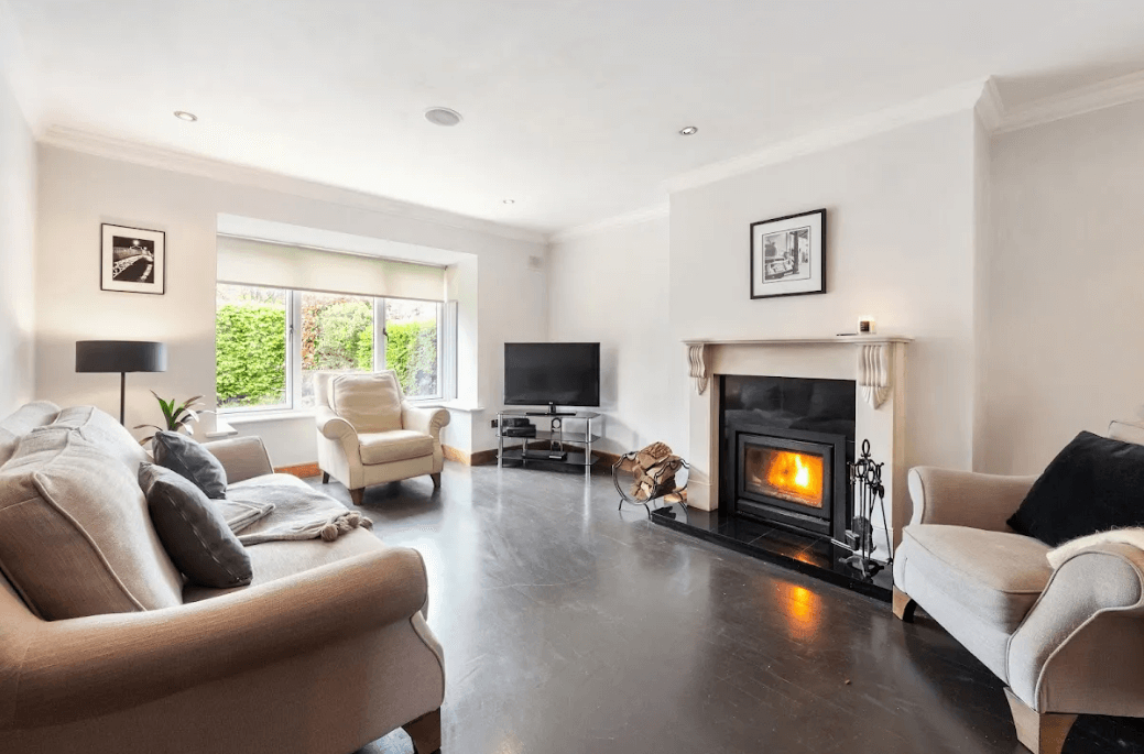 11 Glencairn Glade Leopardstown George and Maguire Properties living room with open fireplace, dark timber flooring, large sofa and large window with view of front garden