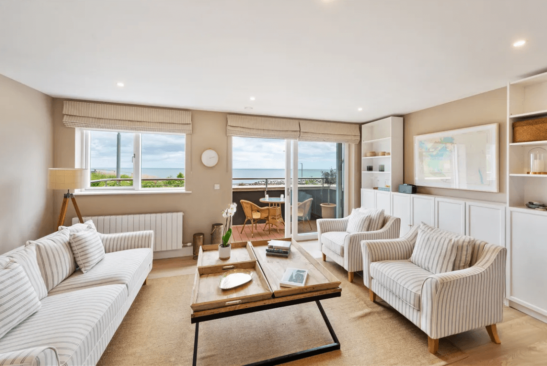 16 The Shore Greystones Wicklow George and Maguire Properties family room with cream sofas and armchairs with marine-type styled decor with a sliding glass door that leads to the balcony area