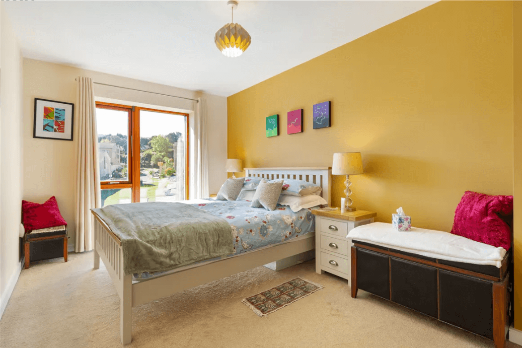 19 Rockbrae Hall Ticknock Hill Sandyford Dublin 18 George and Maguire Properties principal bedroom with large bed, carpeted floor, bedside lockers, mustard-coloured feature wall and large window with views to Dublin mountains