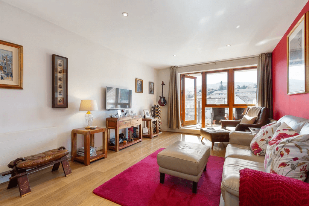 19 Rockbrae Hall Ticknock Hill Sandyford Dublin 18 George and Maguire Properties living room with timber floors, large sofa, large red rug and views through main windows